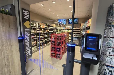 Ein moderner Lebensmittelmarkt mit Regalen voller Getränke und einem Empfangsbereich. Die Atmosphäre ist hell und einladend, mit digitalen Displays an der Decke.