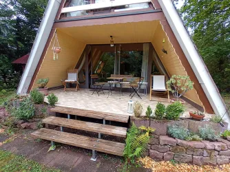 Ein modernes Haus im A-Frame-Stil mit einer einladenden Terrasse. Die Terrasse ist mit Pflanzen dekoriert und bietet Platz für Tisch und Stühle.