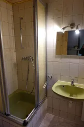 Ein Badezimmer mit einer Dusche und einem Waschbecken. Die Fliesen sind hell und die Beleuchtung ist modern.