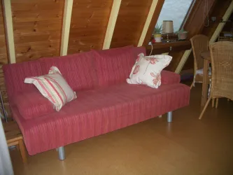 Ein rotes Sofa mit gestreifter Oberfläche und Kissen. Es steht in einem hellen Raum mit Holzverkleidung und einem kleinen Tisch.