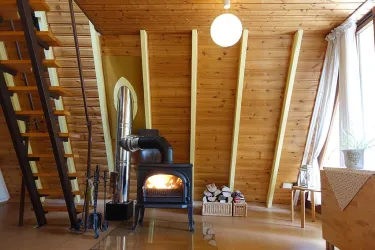 Ein gemütlicher Raum mit Holzvertäfelung und einer modernen Heizung. Eine Treppe führt nach oben, und große Fenster lassen viel Licht herein.