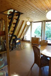 Ein gemütlicher Raum mit Holzverkleidung und großen Fenstern. Im Mittelpunkt steht ein Ofen und ein Tisch mit Stühlen.