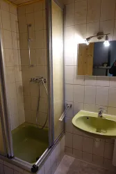 Ein kleines Badezimmer mit einer Duschkabine und einem Waschbecken. Die Wände sind gefliest und die Farben sind hell und neutral.