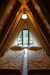 Ein gemütliches Zimmer mit zwei Einzelbetten und einer hohen, spitz zulaufenden Decke. Große Fenster bieten einen Blick auf die Natur draußen.