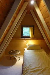 Ein gemütliches Zimmer mit einem Einzelbett und hellem Holzinterieur. Ein Fenster mit Vorhang lässt Tageslicht hereinfällt und schafft eine einladende Atmosphäre.