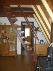 Eine Treppe aus Holz mit modernen Stufen führt in den oberen Bereich des Raumes. Im Hintergrund sind Möbel und Dekorationen sichtbar, die ein gemütliches Wohnzimmer schaffen.