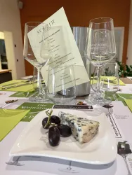 Ein gedeckter Tisch mit Weingläsern, einem Menü und einer kleinen Vorspeise. Auf dem Teller liegen Käse und Trauben.