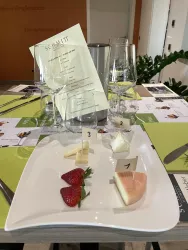 Ein eleganter Tisch mit mehreren Weingläsern und einem Menü auf grünem Untergrund. Auf dem Teller befinden sich verschiedene Käsestücke und Erdbeeren, nummeriert für die Verkostung.