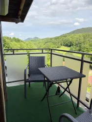 Ein schöner Balkon mit einem Tisch und Stühlen. Im Hintergrund erstrecken sich grüne Hügel und Bäume.