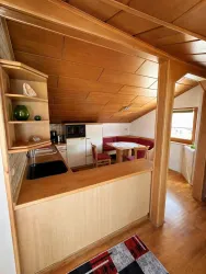 Eine gemütliche Küchenzeile im Dachgeschoss mit Holzdecke und Essbereich. Die Einrichtung ist einfach und funktional, mit einem kleinen Tisch und Stühlen.