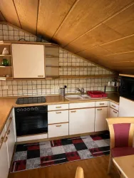 Eine gemütliche Küche mit Holzdecke und modernen Geräten. Der Boden ist mit einem modernen Teppich in Schwarz-Rot gestaltet.
