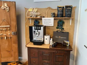 Eine Kaffeestation mit einer modernen Maschine und verschiedenen Kaffeepäckchen. Im Hintergrund hängt ein dekoratives Jutesack-Element mit der Aufschrift "Coffee".