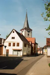 Eine charmante Straße mit traditionellen Häusern und einem hohen Kirchturm. Der Himmel ist klar und blau.