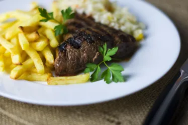 Ein Teller mit gegrilltem Fleisch, Pommes frites und Reis. Das Gericht ist mit frischer Petersilie garniert.