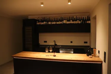 Eine moderne Küche mit einem Holzarbeitsplatz und einem Regal voller Weinflaschen. Im Vordergrund stehen zwei Gläser und eine Flasche Wein.