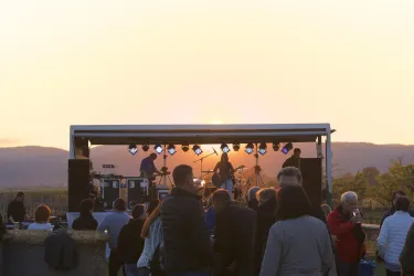 Ein Live-Konzert im Freien bei Sonnenuntergang. Die Zuschauer genießen die Musik vor einer Bühne mit Band.