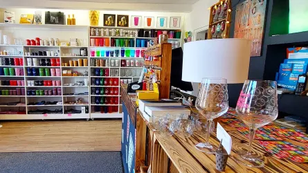 Ein gemütlicher Laden mit bunten Bastelmaterialien auf Regalen. Auf dem Tisch stehen Gläser und eine Lampe.