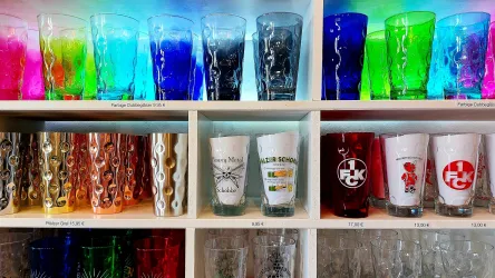 Eine Sammlung von bunten Trinkgläsern in verschiedenen Farben. Die Gläser sind ordentlich in Regalen angeordnet.