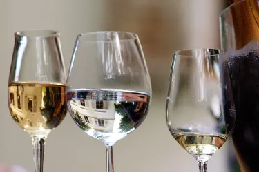 Drei Weingläser mit verschiedenen Getränken stehen auf einem Tisch. Das Licht spiegelt sich in den Gläsern und schafft eine angenehme Atmosphäre.