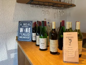 Eine Vielzahl von Weinflaschen steht auf einer Holzoberfläche. Daneben befindet sich ein Schild mit dem Spruch über Wein und Frühstück.