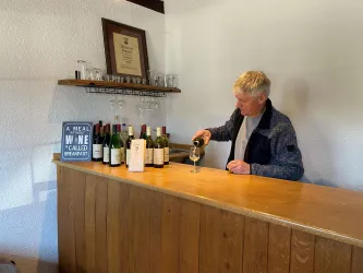 Eine Person schenkt Wein hinter einem Bartresen ein. Im Hintergrund sind Flaschen und eine Auszeichnung sichtbar.