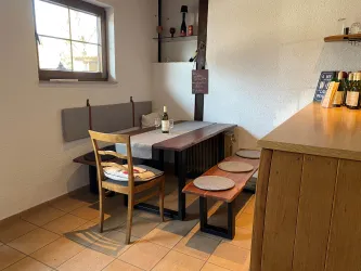 Ein gemütlicher Essbereich mit einem Tisch und Stühlen. Auf dem Tisch steht eine Flasche Wein in einem ruhigen Raum.