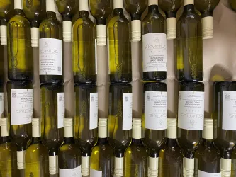 Eine Wand mit Flaschen weißem Wein, die ordentlich nebeneinander angeordnet sind. Die Etiketten zeigen verschiedene Weinsorten und -marken.