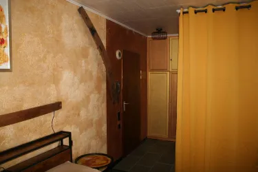Ein einfacher Raum mit einem Holzbett und einer gelben Vorhang. An der Wand ist ein brauner Farbton und ein Schrank befindet sich in der Ecke.