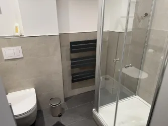 Ein modernes Badezimmer mit einer Dusche und einer Toilette. Die Wände sind mit Fliesen in neutralen Farben gestaltet.