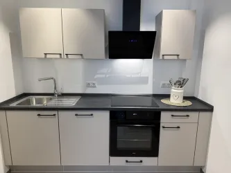 Eine moderne Küche mit hellen Schränken und einer dunklen Arbeitsplatte. Sie ist ausgestattet mit einem Spülbecken, einem Herd und einem Backofen.