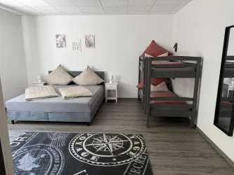 Ein gemütliches Schlafzimmer mit einem Doppelbett und einem Etagenbett. Der Raum ist hell und modern eingerichtet mit einem Teppich und Wandbildern.