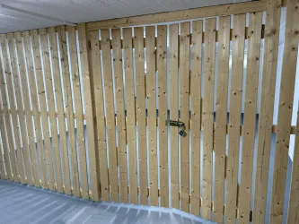 Eine Holzwand mit vertikalen Latten und einer Tür. Die Oberfläche wirkt hell und natürlich.