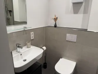 Ein modernes Badezimmer mit einem Waschbecken und einer Toilette. Eine dezente Dekoration mit einer Blume sorgt für einen stilvollen Akzent.