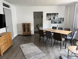 Ein modernes Esszimmer mit einem großen Holztisch und sechs Stühlen. Die Wände sind mit Bildern dekoriert, und ein Teppich liegt auf dem Boden.