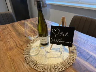 Eine Flasche Wein steht auf einem Tisch zusammen mit zwei Gläsern und einem Willkommensschild. Der Tisch hat eine natürliche Holzoberfläche und ist ansprechend dekoriert.