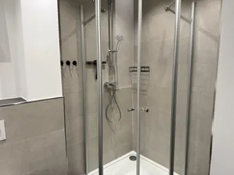 Eine moderne Dusche mit Glaswänden und einer Handbrause. Die Wände sind in neutralen Farbtönen gehalten.