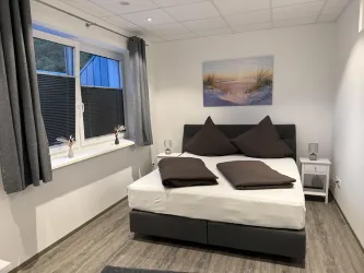 Ein modernes Schlafzimmer mit einem großen Bett und grauen Vorhängen. An der Wand hängt ein Bild einer Winterlandschaft.