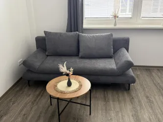Ein modernes graues Sofa steht in einem hellen Raum. Neben dem Sofa gibt es einen runden Tisch mit einer kleinen Vase und Dekoration.