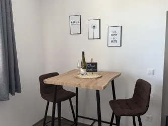 Ein stilvoller Essbereich mit einem hohen Tisch und zwei Stühlen. An der Wand hängen dekorative Bilder.