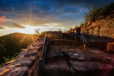 Eine alte Ruine im Sonnenuntergang mit sanften Lichtstrahlen. Im Hintergrund sind sanfte Hügel und ein klarer Himmel zu sehen.