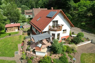 Ein modernes Haus mit rotem Dach inmitten einer grünen Gartenlandschaft. Der Garten ist mit verschiedenen Pflanzen und einem gemütlichen Sitzbereich gestaltet.