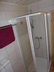 Eine moderne Dusche mit Glasabtrennung in einem gefliesten Badezimmer. Ein rotes Handtuch hängt an der Stange daneben.