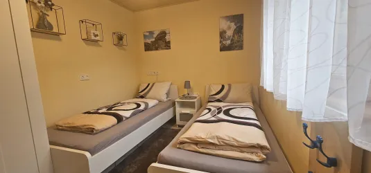 Ein gemütliches Schlafzimmer mit zwei Einzelbetten und einem kleinen Nachttisch. Die Wände sind hell gestrichen und mit einigen Bildern dekoriert.