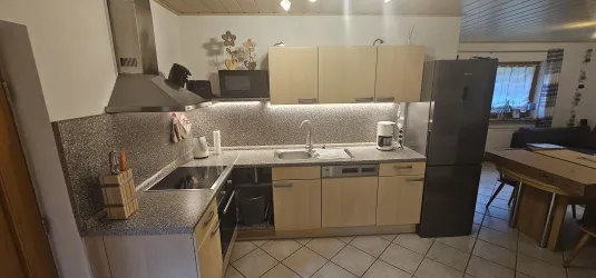 Eine moderne Küche mit Holzschränken und einer grauen Arbeitsplatte. Die Ausstattung umfasst einen Herd, einen Kühlschrank und eine Spüle.