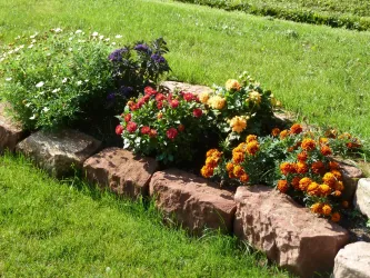 Ein blühendes Blumenbeet mit bunten Blumen in verschiedenen Farben. Es ist von großen Steinen umgeben und liegt im grünen Gras.