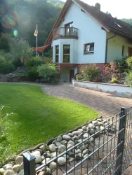 Ein schönes Haus mit einem gepflegten Garten und einem gepflasterten Weg. Es gibt Pflanzen und einen Balkon, auf dem die deutsche Flagge weht.
