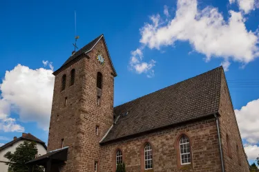 Eine alte Steinkirche mit einem hohen Turm und einem großen Zifferblatt. Der klare blaue Himmel und die weißen Wolken verleihen der Szene eine ruhige Atmosphäre.