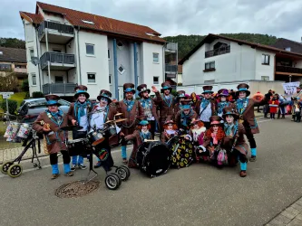 Eine Gruppe von Menschen in bunten Kostümen steht auf einer Straße. Sie halten Musikinstrumente und lächeln fröhlich in die Kamera.