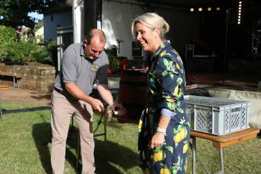 Ein Mann und eine Frau stehen in einem Garten. Der Mann hält einen Fisch, während die Frau lächelt und zuschaut.