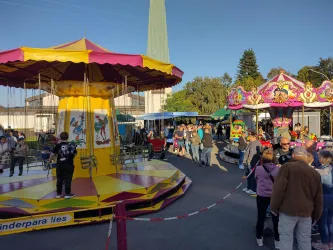 Ein Jahrmarkt mit bunten Fahrgeschäften und vielen Menschen. Die Atmosphäre ist lebhaft und fröhlich.
